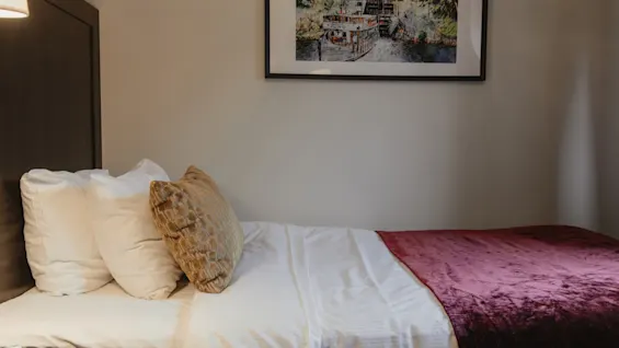 A cozy bed with white linens and a purple throw, beneath a framed artwork, in a room at Home Hotel Kung Oscar. 🛏️🖼️