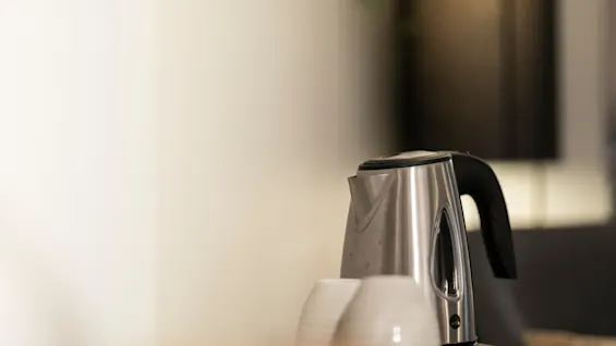 En vannkoker i rustfritt stål og kopper på et brett, klar for varme drikker.