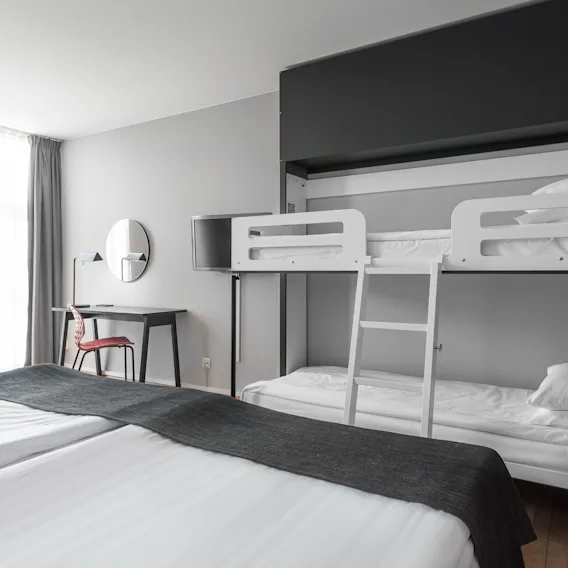 Ljust hotellrum med en dubbelsäng och en våningssäng i modern stil.