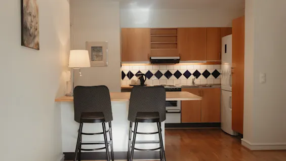 Et varmt og indbydende køkkenområde med træskabe, et karakteristisk flisebelagt stænkpanel og en morgenmadsbar med to skamler.