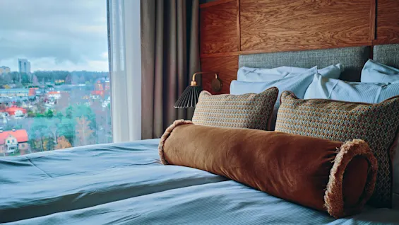 En komfortabel hotellseng med utsikt over et bylandskap utenfor vinduet, noe som antyder et avslappende opphold.
