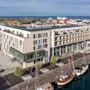 Moderni hotellirakennus lasijulkisivulla, josta on näkymä satamaan, jossa on useita veneitä, kaupunki ja meri taustalla.