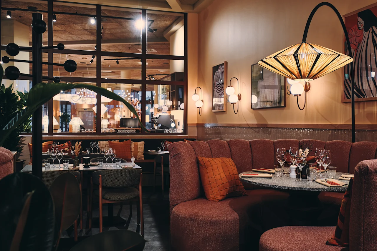 Et stilig restaurantinteriør med dekkede bord, komfortable sitteplasser og varm belysning, som skaper en innbydende spiseatmosfære.