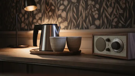 A cozy scene with a kettle, two cups, a lamp, and a vintage radio. The radio displays MODEL TWO M and HOME AUDIO.