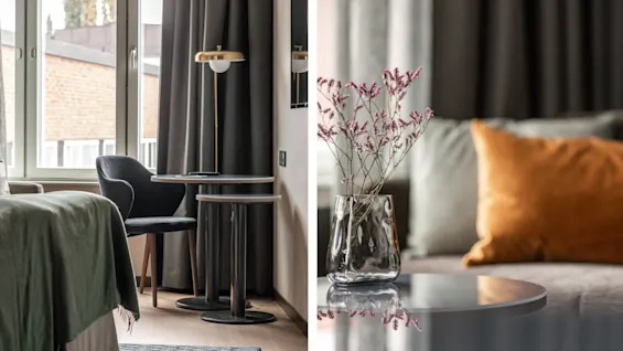 En mørk stol og et rundt bord står ved et vindue med grå gardiner i et rum. En vase med lyserøde blomster står på et bord nær farvede puder.