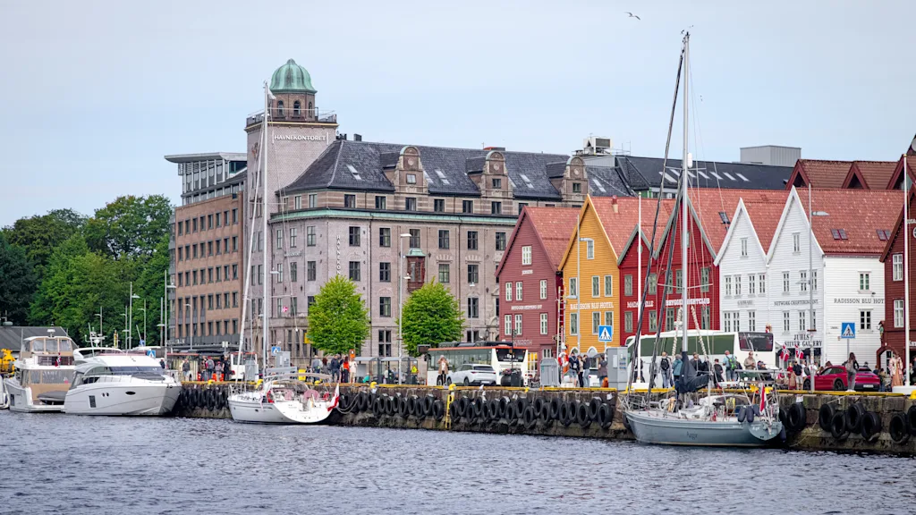 Naturskøn havn med historiske farverige træhuse og både fortøjet langs kajen.