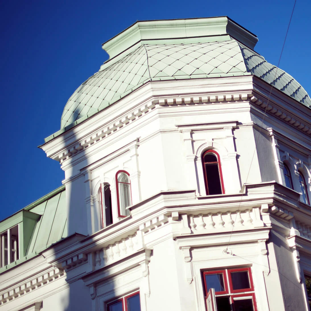 En vit byggnad med en grön kupol under en klarblå himmel, inramad av grenar.