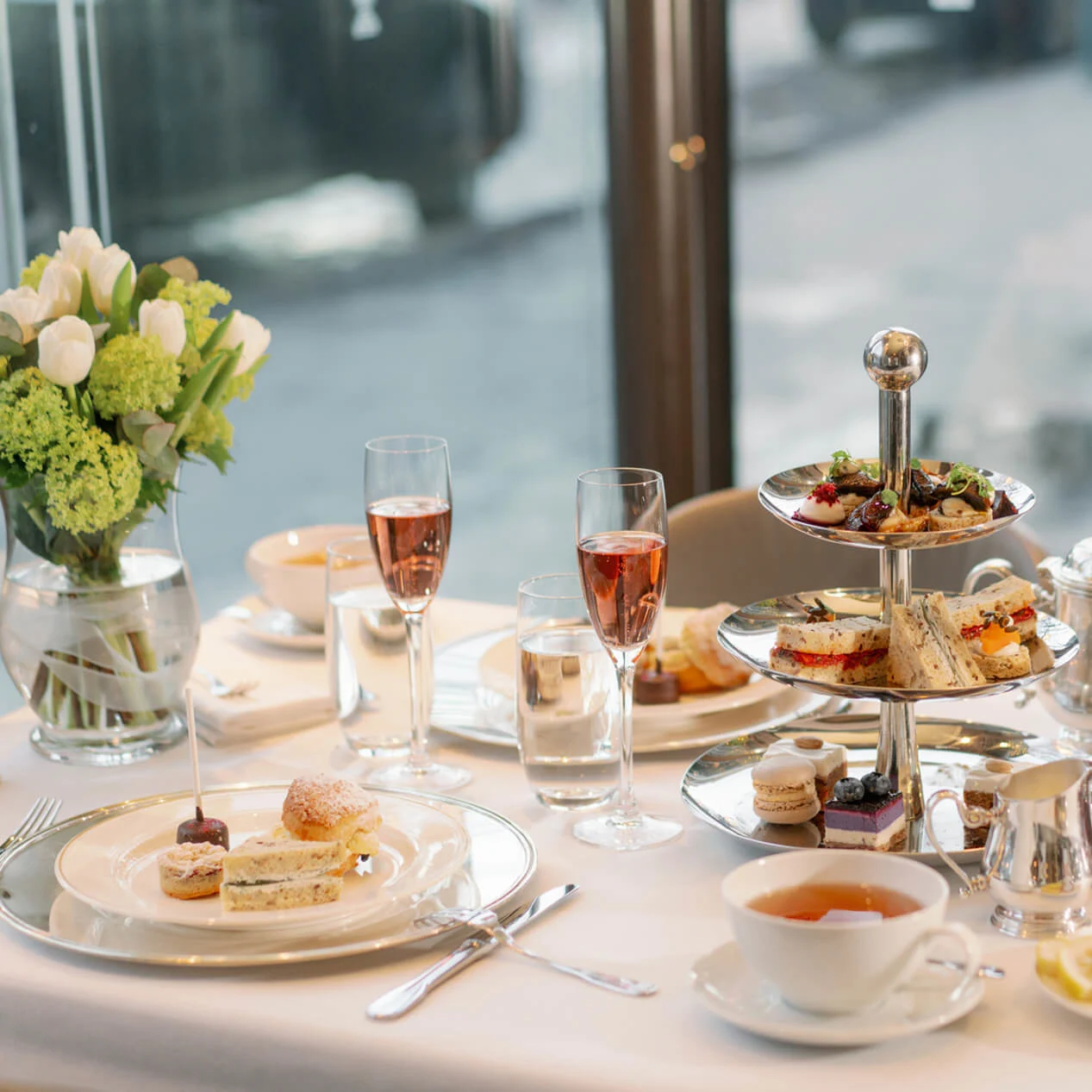 An elegant afternoon tea setup with a three-tiered serving stand filled with sandwiches and pastries, and accompanying beverages on a table at Hotel Kämp in Helsinki.