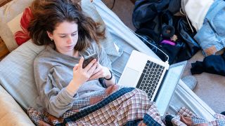 Teenager in bed with phone and laptop