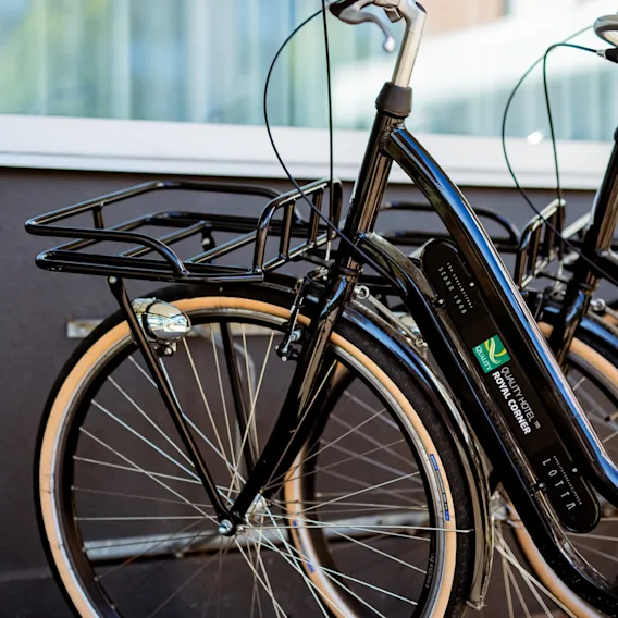 En svart cykel från Quality Hotel Royal Corner, med en framkorg och ljusa däck, parkerad och redo för utforskning.