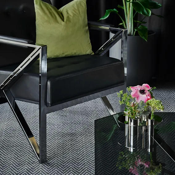 En elegant hotellounge med en bekväm fåtölj, en livfull grön kudde och ett fräscht blomsterarrangemang på ett glasbord.