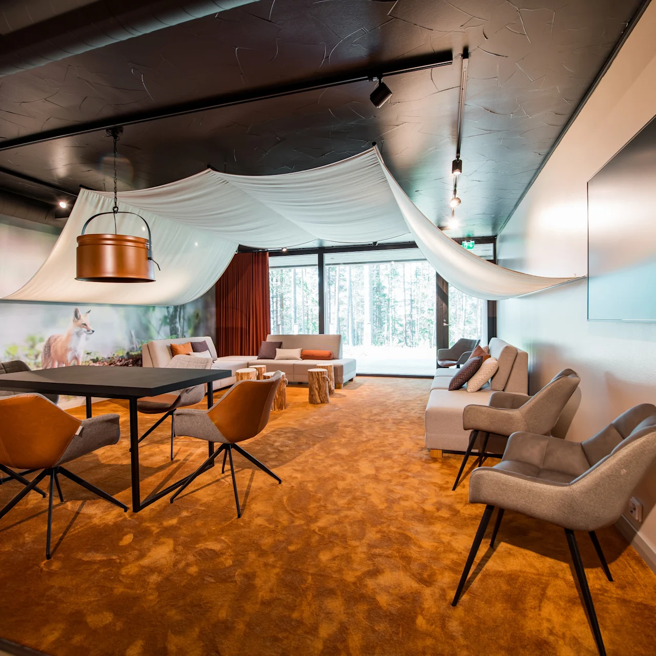 A modern meeting room with a large table and chairs, soft lighting, and abstract ceiling drapes, set against a forest-themed wallpaper. Bright natural light streams through large windows.