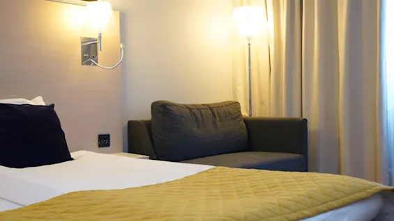 Et komfortabelt Standardværelse på Quality Hotel Sundsvall, med en seng med gult sengetæppe og en grå sofa, varmt belyst.