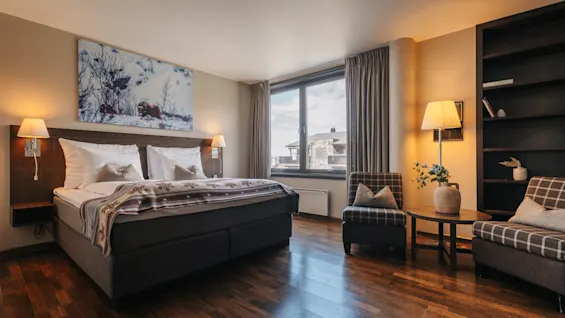 Ett rymligt hotellrum med en stor dubbelsäng, trägolv och en mysig sitthörna vid fönstret.