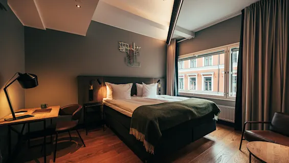 A cozy hotel room with a comfortable bed, a desk for working, and a window offering a view of the city.