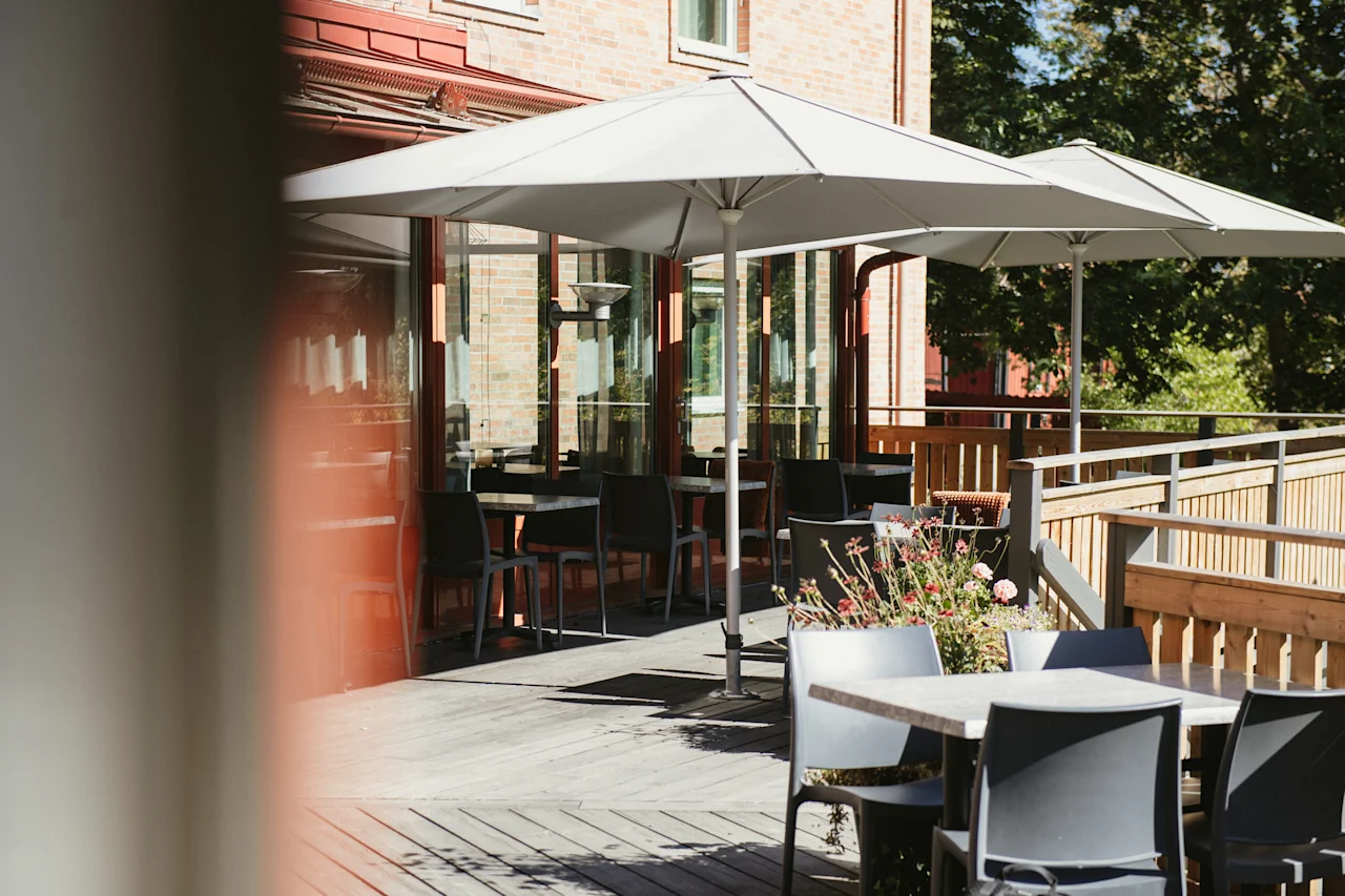 En inbjudande uteplats med bord, stolar och stora parasoller, perfekt för att äta eller koppla av en solig dag.