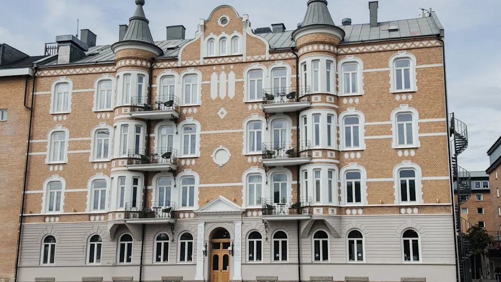 En rikt utsmyckad fyravåningsbyggnad med rundade torn och flera fönster visar en klassisk arkitektur. Balkonger på varje våning är försedda med räcken, i en stadsmiljö.