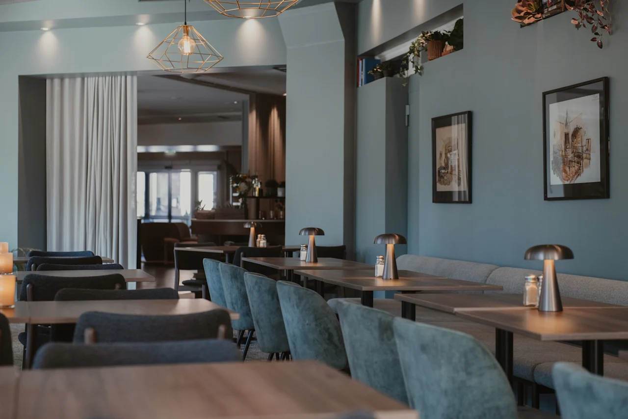 En modern restauranginredning med prydligt arrangerade bord och stolar, upplyst av stilrena taklampor och bordslampor.