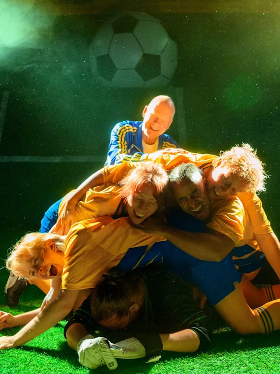 Fotbollsspelare som firar i en jublande hög på gräset under grönt ljus.