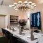 A dining table is elegantly set with folded napkins and wine glasses, surrounded by black chairs. A chandelier hangs overhead in a modern room with artwork on the wall.
