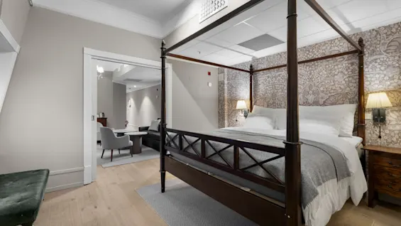 A charming hotel suite with a grand four-poster bed and an inviting separate living space, perfect for relaxation.