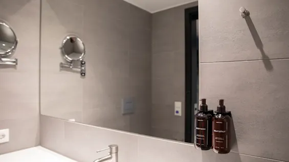 Moderne bad med stort speil som reflekterer vask, kran og to veggmonterte dispensere merket BODY WASH og BODY LOTION.