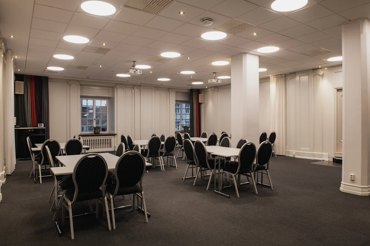 Ett rymligt konferensrum på Home Hotel Grand, Helsingborg, möblerat med flera bord och stolar för ett möte eller evenemang.