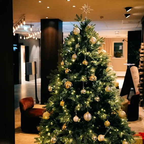 Et høyt juletre pyntet med gullkuler, varme lyslenker og en stjerne i toppen i en hotellobby.