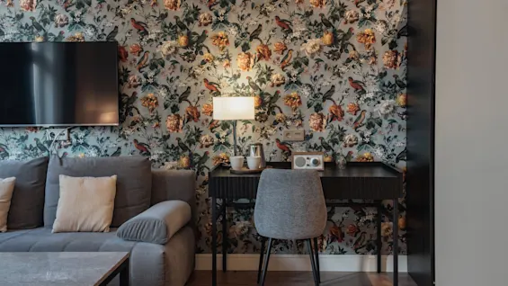 Et hyggeligt hotelværelse på Home Hotel Norre Park i Halmstad med blomstret tapet, en komfortabel sofa og et funktionelt skrivebordsområde.