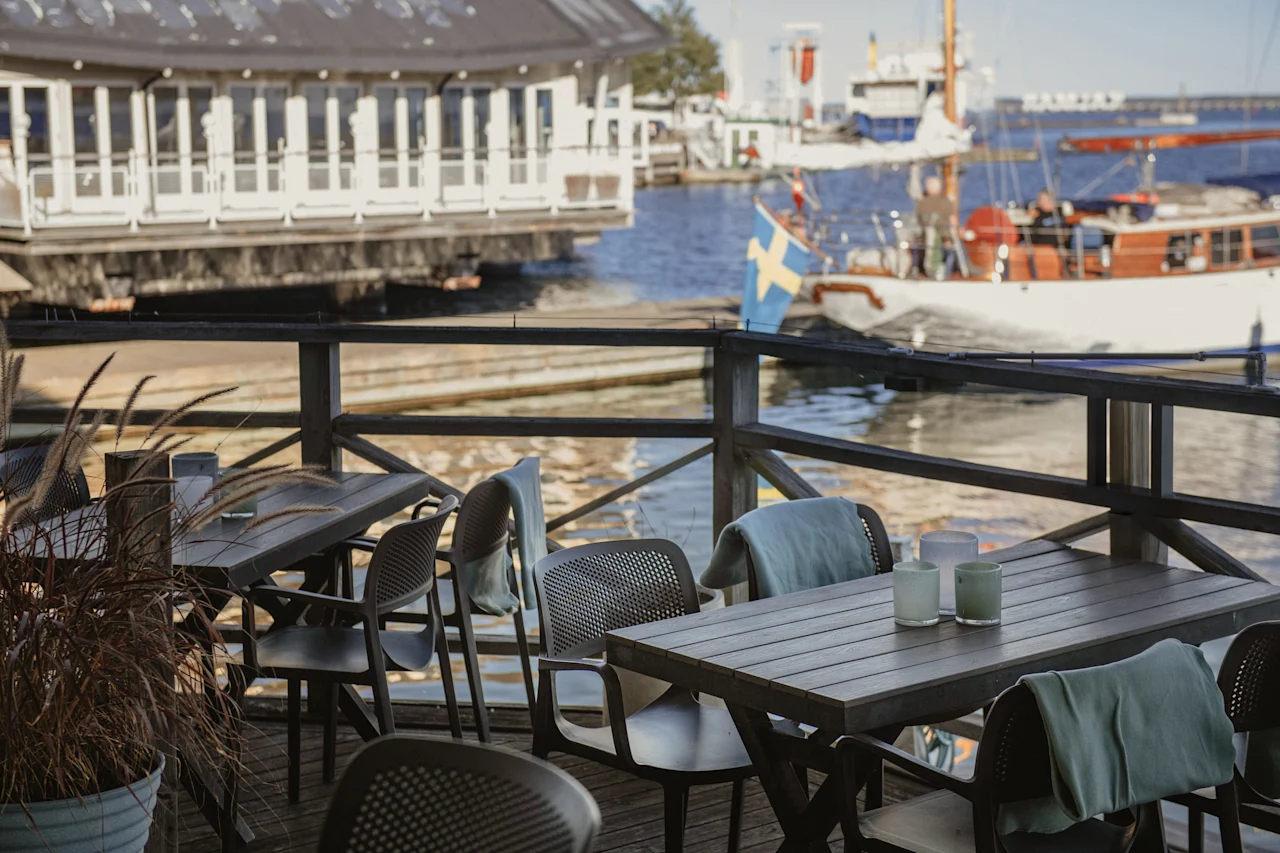 En rolig udendørs spiseplads på et trædæk, der tilbyder malerisk udsigt over en havn fyldt med både.