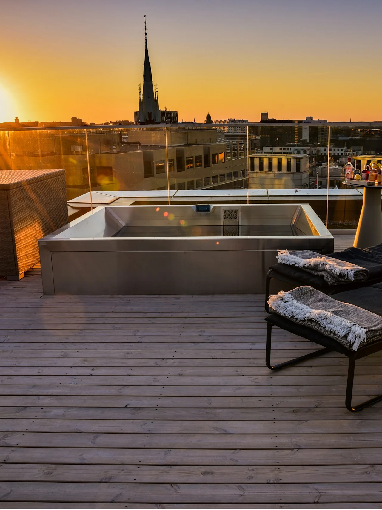 Rooftop terrace at sunset with a hot tub, lounge chairs, and city views. Perfect for relaxation and enjoying the evening.
