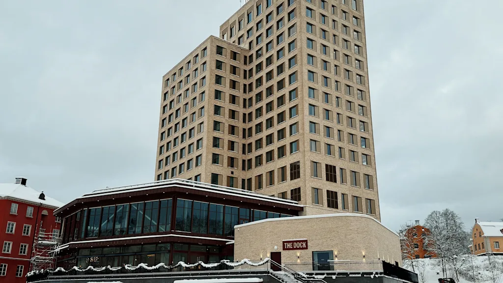 En moderne, høy bygning med en lavere del, med et skilt som leser THE DOCK, omgitt av snø en overskyet vinterdag.