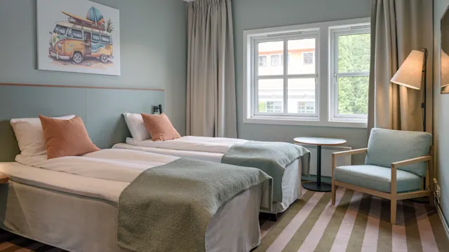 To enkeltsenger er pent arrangert med grønne tepper i et koselig, moderne soverom. Et surfbil-maleri henger på veggen ved siden av et vindu med beige gardiner.