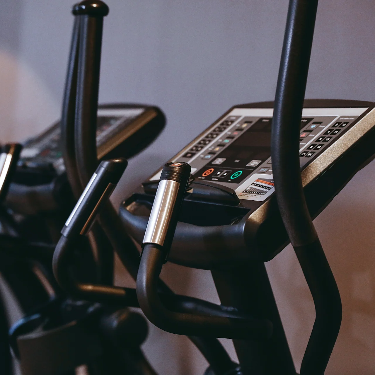Exercise bikes with digital displays stand ready for use in a gym setting, surrounded by neutral-colored walls.