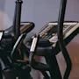 Exercise bikes with digital displays stand ready for use in a gym setting, surrounded by neutral-colored walls.