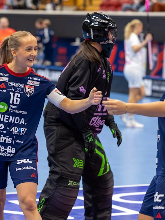 Innebandyspelare firar på planen, med en spelare nummer 16 och en annan nummer 2, som interagerar med målvakten.