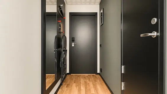 Modern hotel hallway with wooden flooring, dark doors, and a large mirror on the wall.