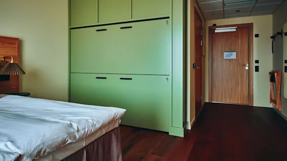 Et komfortabelt hotellrom med en pent oppredd seng, en moderne grønn garderobe og en innbydende tredør.
