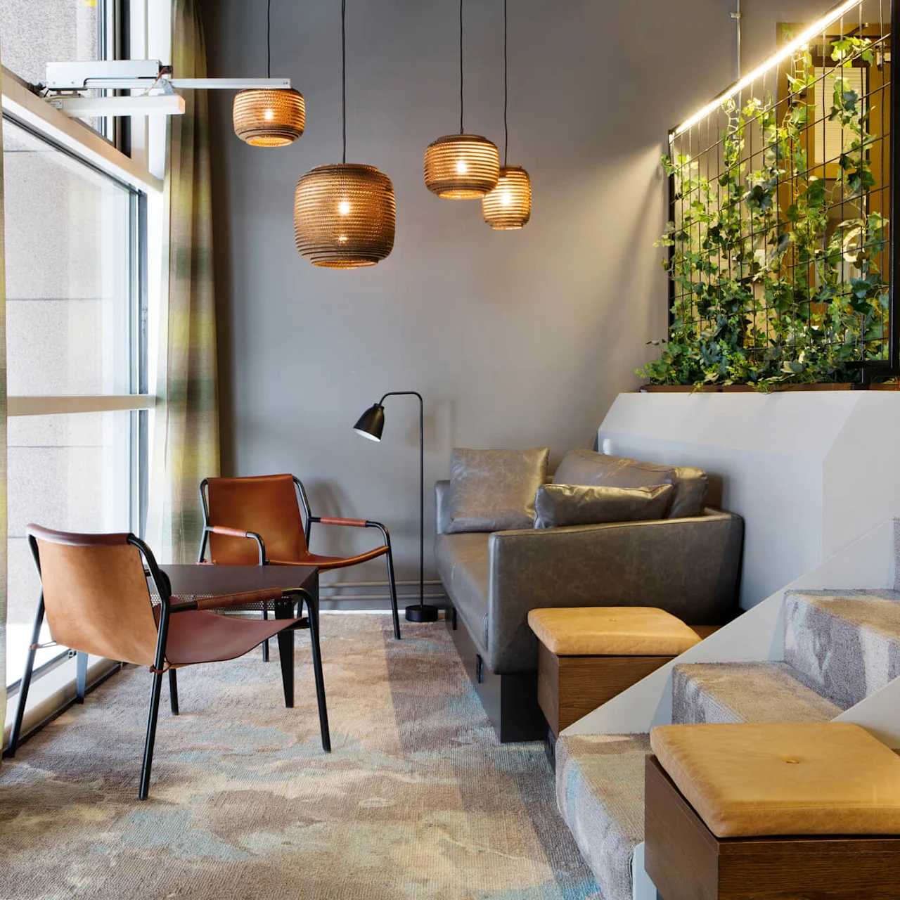 En moderne loungesone med stilige sitteplasser, hengende lamper og en vertikal hage ved siden av et vindu, som skaper en koselig atmosfære.