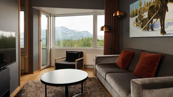 A cozy living room with modern furniture and large window revealing a mountainous landscape.