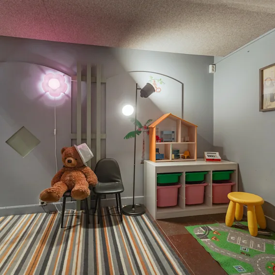 Et hyggeligt legeområde for børn med en bamse, dukkehus og legemåtte, der inviterer til fantasifuld leg.