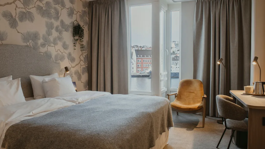 Et hyggeligt hotelværelse med en stor seng, et skrivebord og et vindue med udsigt over en by og vand.