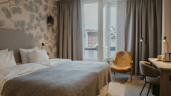 Et hyggeligt hotelværelse med en stor seng, et skrivebord og et vindue med udsigt over en by og vand.