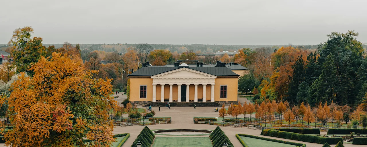 Suuri pylväsrakennus avautuu muodolliseen puutarhaan, jossa on syksyisiä puita ja leikattuja pensasaitoja Uppsalan kasvitieteellisessä puutarhassa.