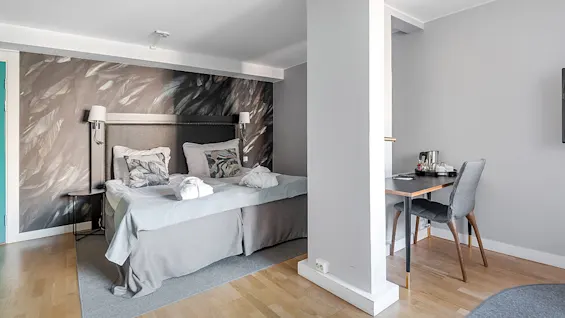 A tidy bedroom with a double bed and decorative pillows, featuring an accent wallpaper. A dining area with a small table and chair is also visible.