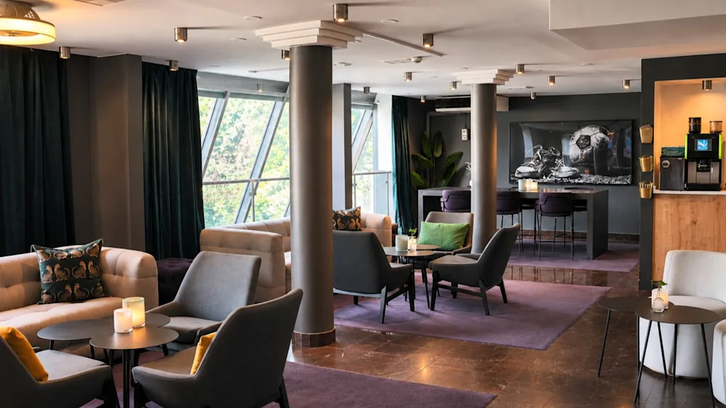 Lämmin ja kutsuva hotellin aula, joka on suunniteltu rentoutumiseen ja sosiaalisiin tapaamisiin, mukavilla istuimilla ja modernilla baarilla.