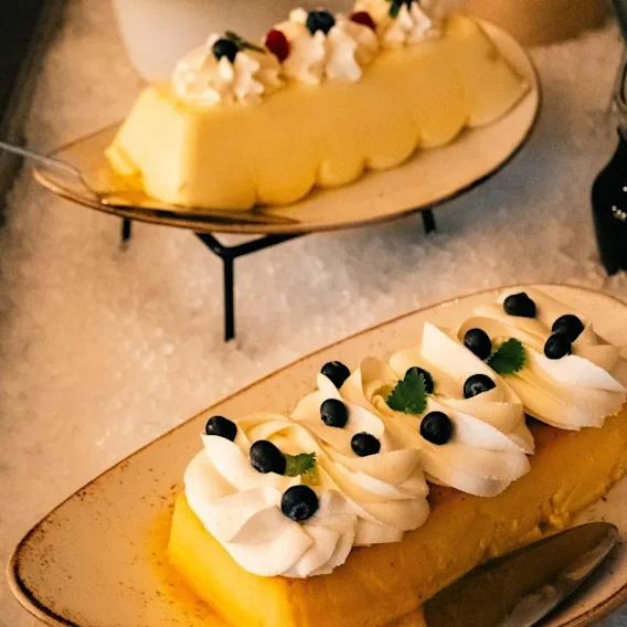 Dessertanretninger pyntet med krem, blåbær, bringebær og mynteblader på fat over knust is.