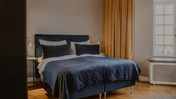 Ett mysigt hotellrum på Home Hotel Grand, Helsingborg, med en bekväm säng med blå sängkläder och varm belysning.