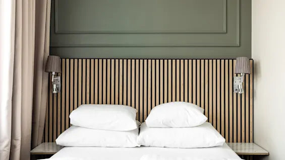 Kutsuva sänky valkoisilla lakanoilla, puinen sängynpääty ja vihreä seinä Comfort Hotel Linkoping Cityssä.