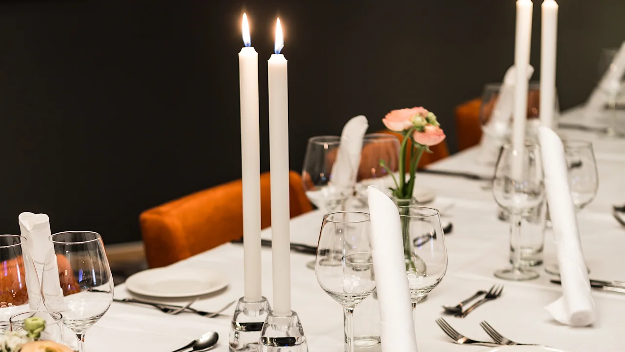 Et vakkert dekket middagsbord med hvit duk, tente lys, elegante glass, bestikk og blomsterarrangementer.